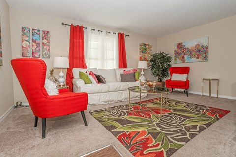 Furnished living room with red seats and white couch, red curtains, and floral rug at Magnolia apartments in Shreveport, LA